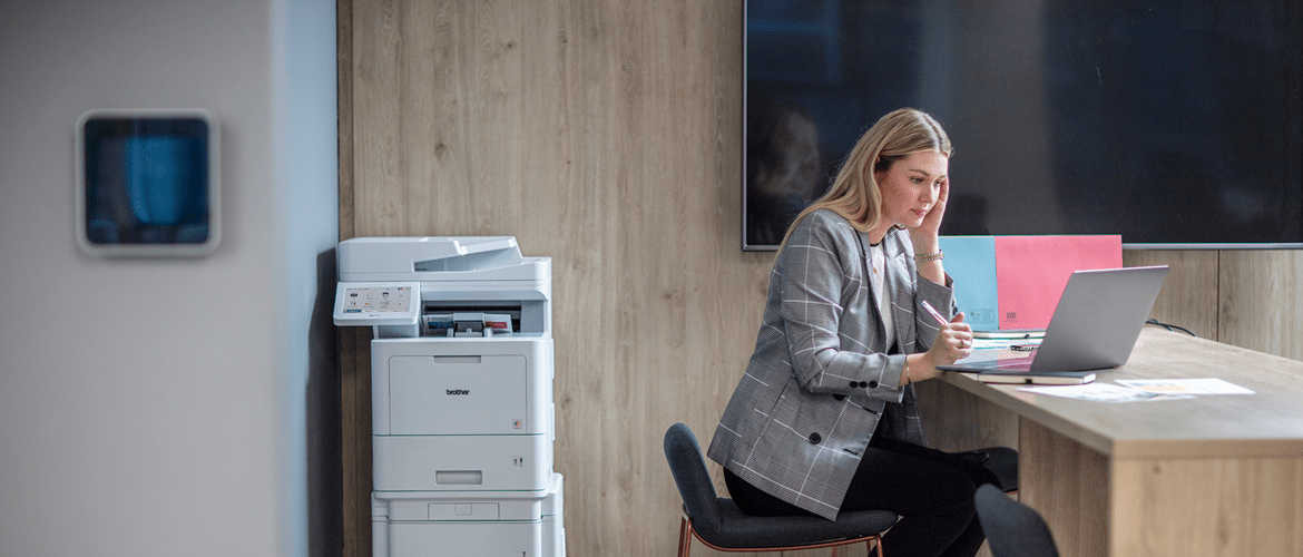 a woman sitting at a desk on a barstool using a laptop