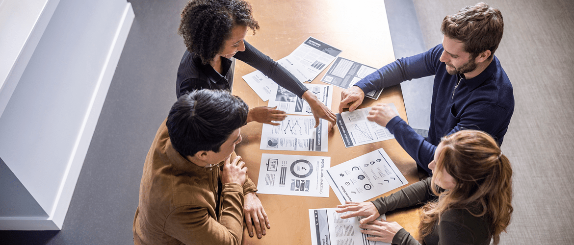 business people gather around a table with paperwork representing Brother's business solutions including Managed Print Services