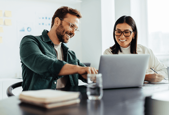 A man dressed in business casual works collaboratively with a woman colleague behind a laptop