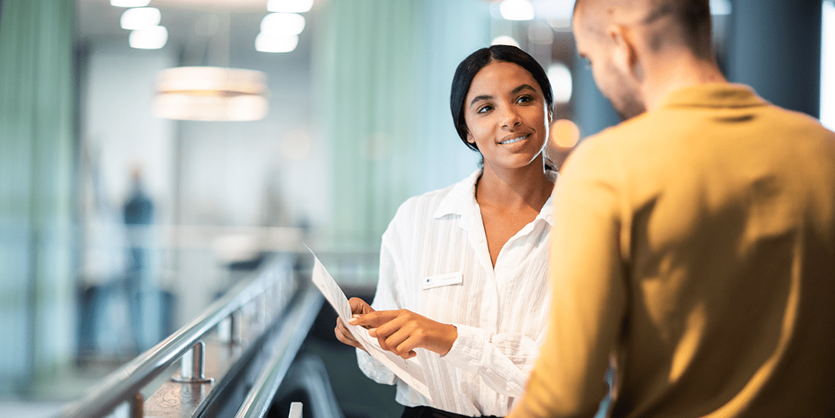 A woman facing a man pointing at a piece of paper discussing business